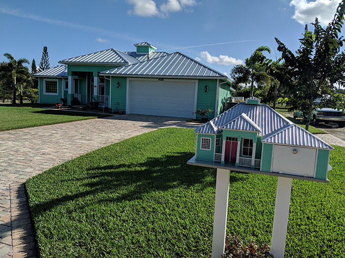 Creative mailbox designed as a miniature house matching the real home behind it on a sunny day with green lawn.