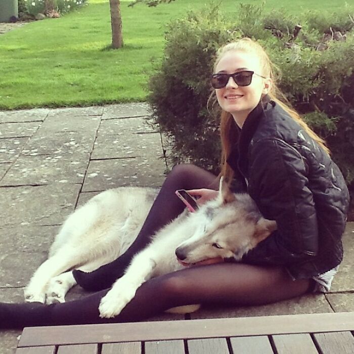Young woman wearing sunglasses sitting outdoors, cuddling a large dog, showing immense love for dogs and pets.