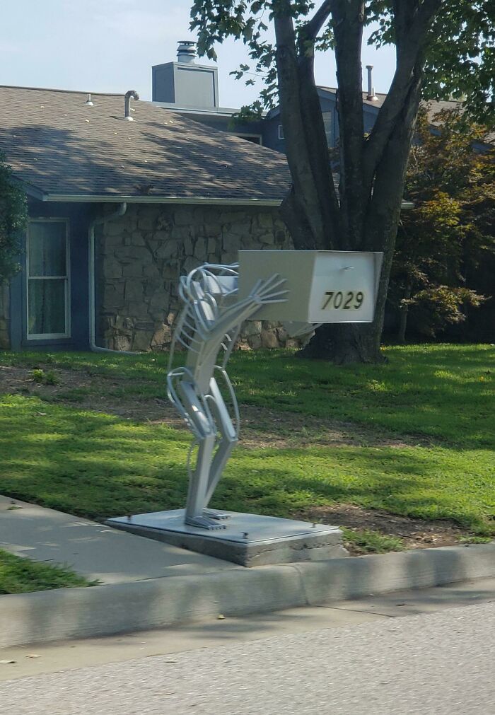 Creative and cool mailbox designed as a metal figure carrying a traditional mailbox on a suburban sidewalk.