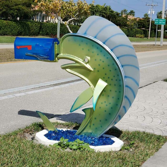 Whimsical fish-shaped mailbox with a blue mail compartment, creatively designed and spotted in a residential area.