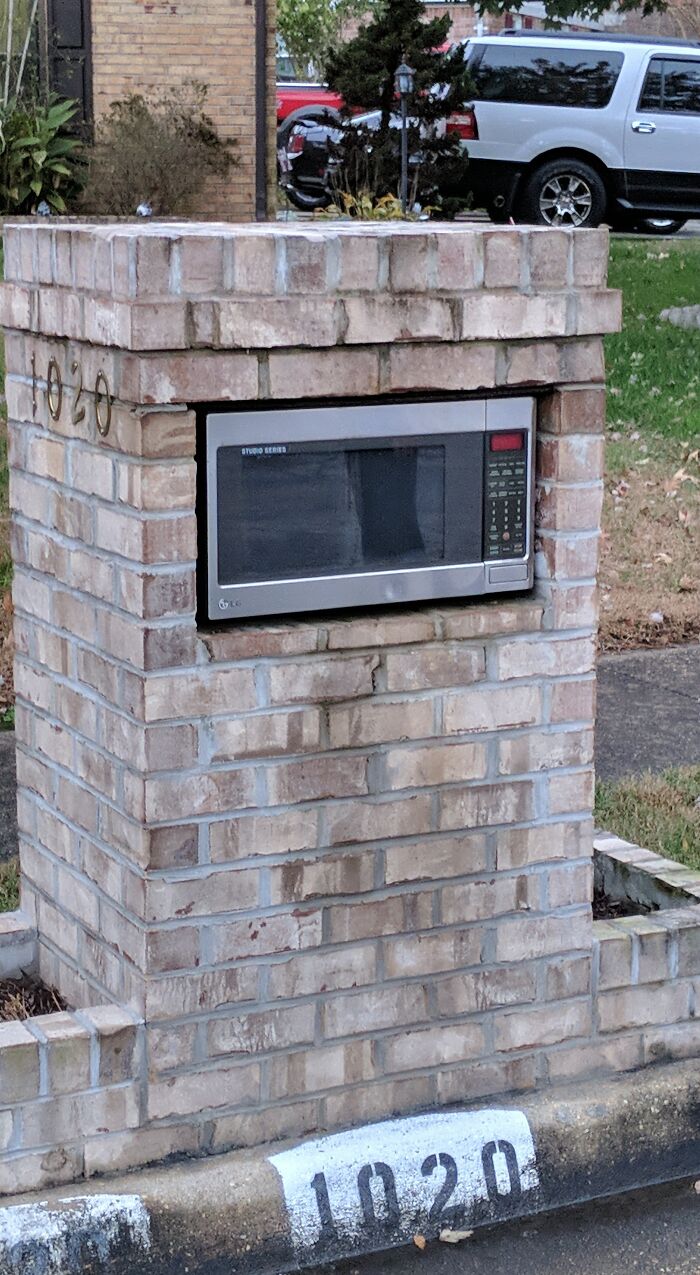 Brick mailbox featuring a microwave oven creatively repurposed as a unique and cool mailbox in a residential area.