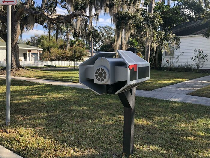 Creative and cool mailbox designed like a spaceship mounted on a black post in a suburban neighborhood.