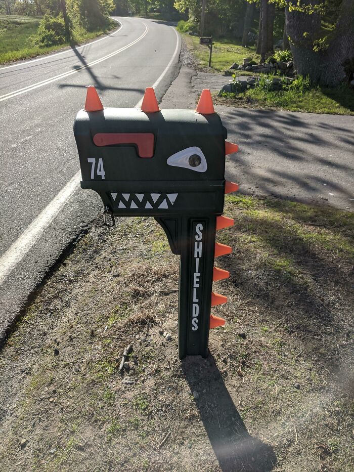 Creative mailbox shaped like a dinosaur with orange spikes, located on a roadside, showcasing cool mailbox design ideas.