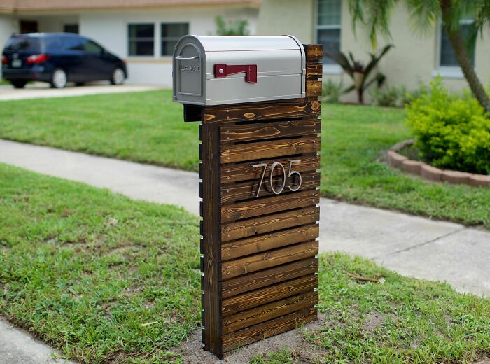 Modern mailbox mounted on a unique wooden stand with house number 705 in a residential neighborhood lawn.