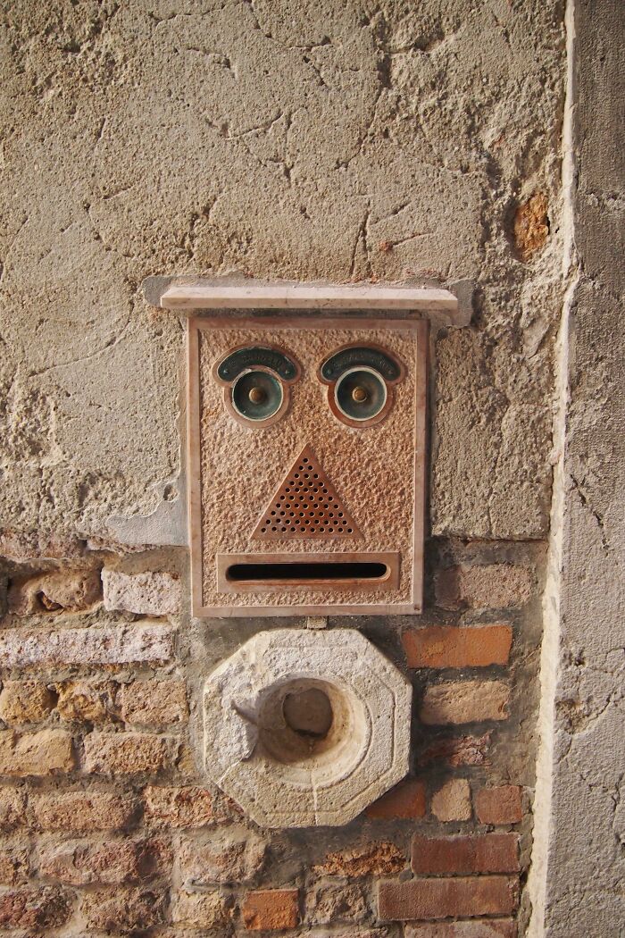 Creative and cool mailbox designed with a face-like structure mounted on an old textured wall outdoors.