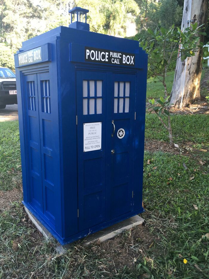 Creative and cool mailbox designed like a classic blue police public call box standing outdoors on grass.