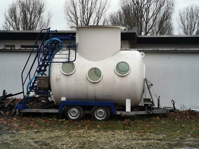 Trailer With A Submarine-Resembling Container With Portholes Parked On The Grounds Of A Public Swimming Pool