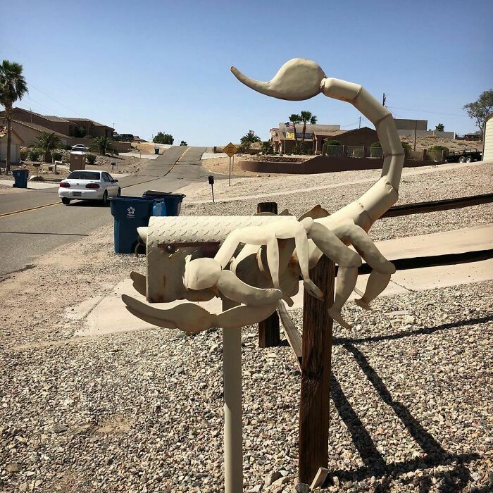 Creative and cool mailbox designed as a large scorpion sculpture on a rural roadside in a sunny neighborhood.