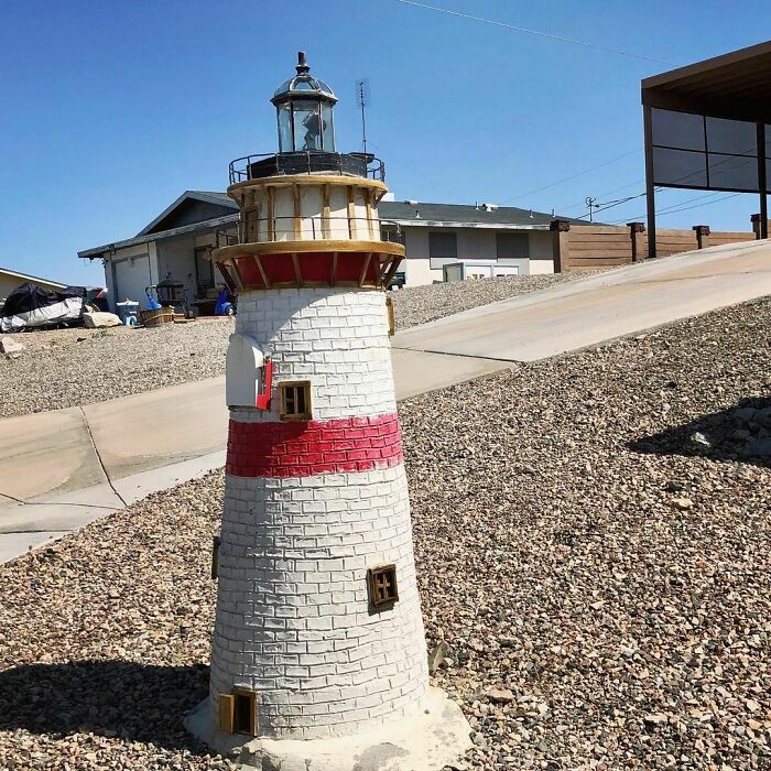 Lighthouse-shaped creative and cool mailbox placed on a rocky yard in a residential neighborhood.