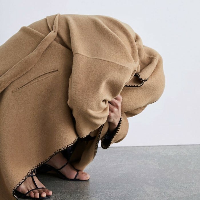 Model in unusual pose wearing a beige coat and sandals, highlighting Zara's unique online shopping challenges.