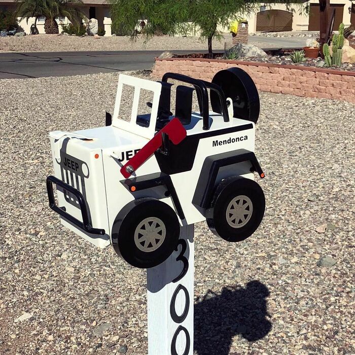 Creative and cool mailbox designed like a white Jeep, mounted on a white post with house numbers in a desert landscape.