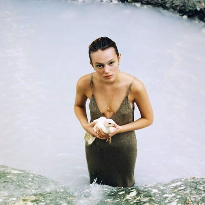 Model in unusual pose standing in water, holding a duck, showcasing Zara's unique style.