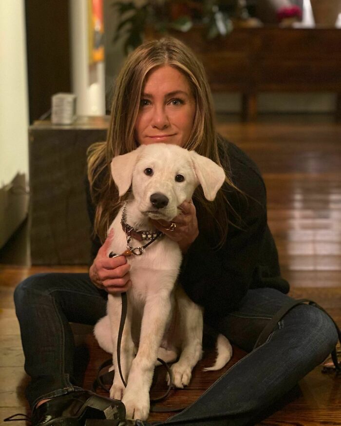 Woman sitting on the floor holding a white puppy, showcasing celebrity love for dogs in a cozy indoor setting.