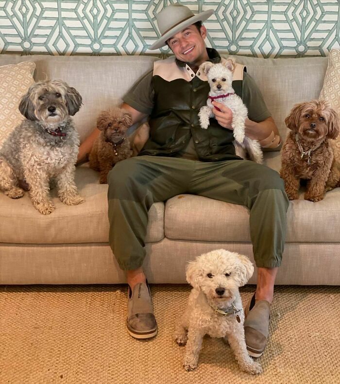 Man sitting on couch with five dogs, showcasing celebrity love for dogs in a cozy home setting.