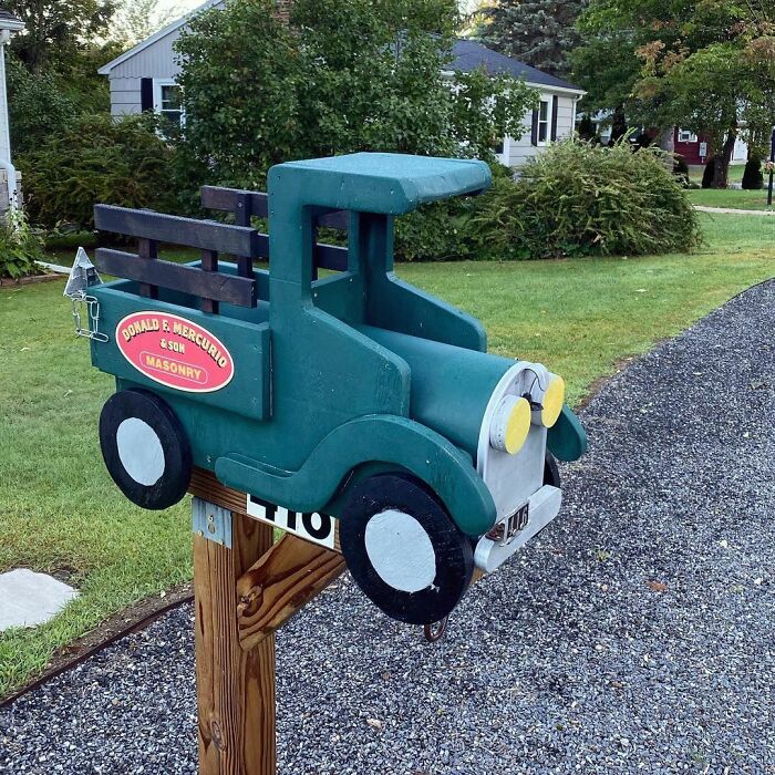 Creative and cool mailbox designed like a vintage green truck mounted on a wooden post in a suburban yard.