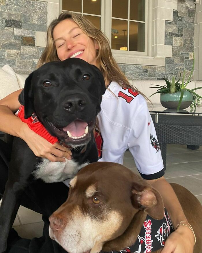 Woman happily hugging two dogs indoors, showcasing celebrities love for dogs with joyful pets wearing bandanas.