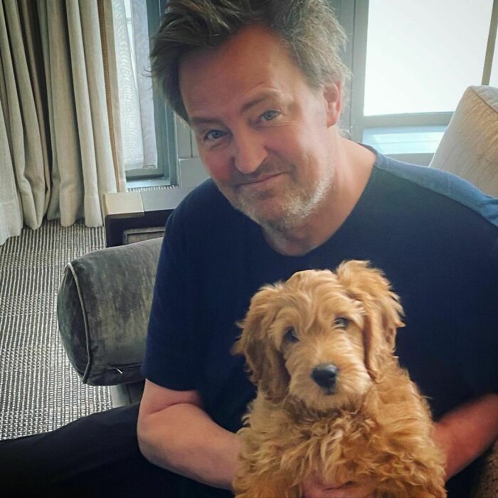 Man sitting indoors holding a fluffy dog, showcasing celebrities love for dogs in a cozy home setting.