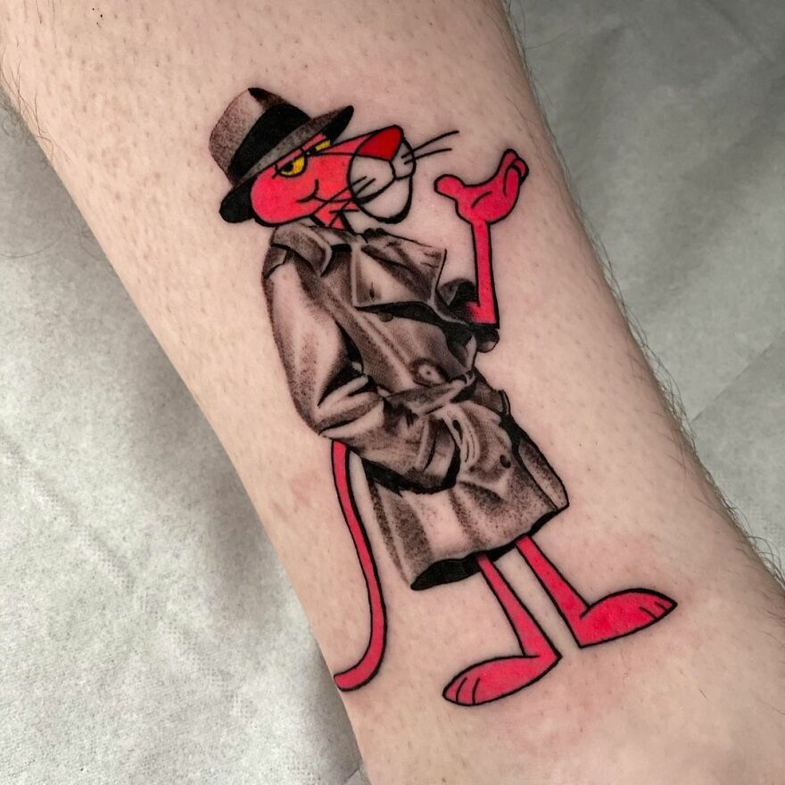 Tattoo of a cartoon character blends two styles: grayscale trench coat and vibrant red features, showcasing unique artistry.