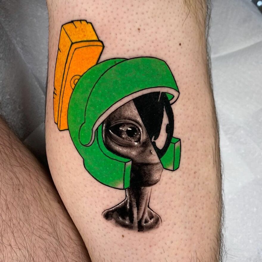 Mixed style tattoo depicting an alien and cartoon character helmet design by Mat Rule.