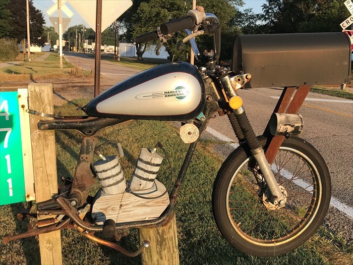 Creative mailbox designed like a vintage Harley Davidson motorcycle mounted beside a rural road.