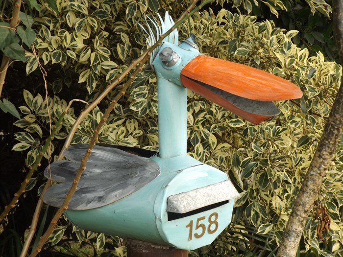 Creative and cool mailbox shaped like a colorful bird with an orange beak and the number 158 in a garden setting.