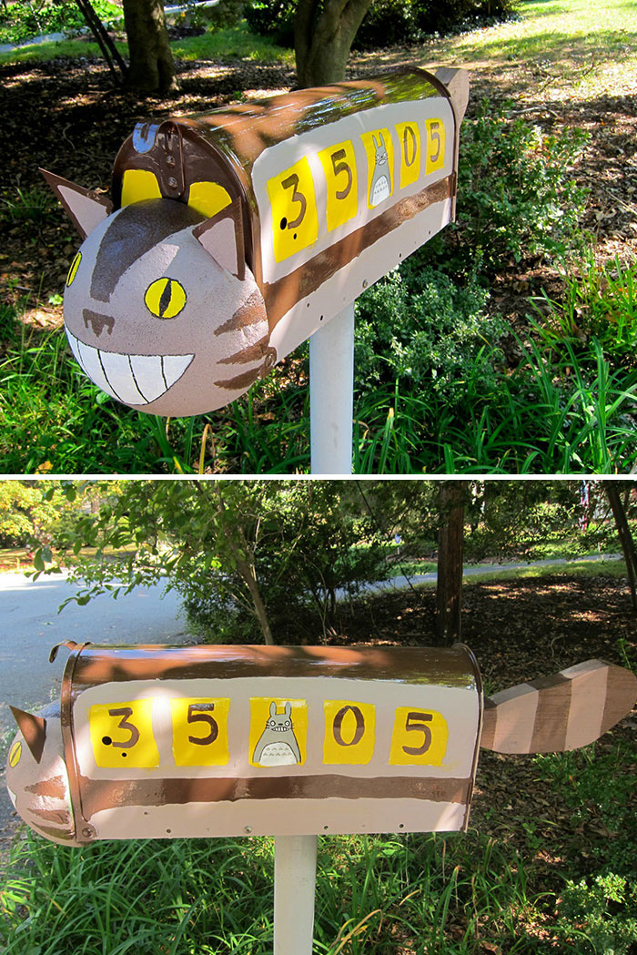 Creative cat-shaped mailbox painted brown and tan with yellow eyes and whimsical details in a natural outdoor setting.