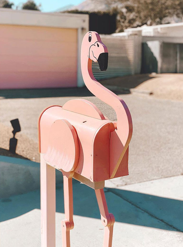 Creative and cool mailbox designed as a pink flamingo standing in a residential driveway on a sunny day.