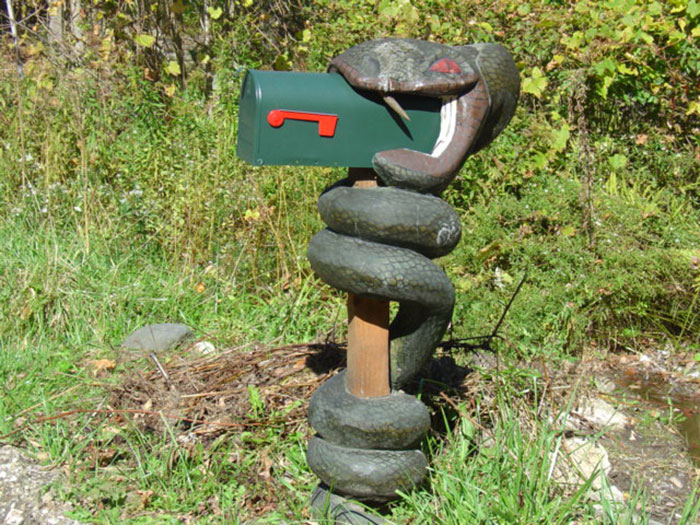 Snake mailbox wrapped around post with green mailbox and red flag in a natural outdoor setting creative mailbox design
