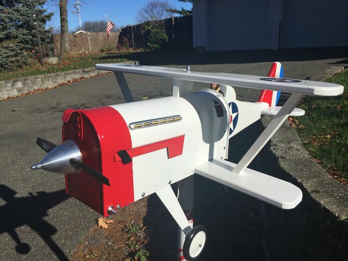 Creative mailbox designed like a vintage airplane with red and white colors spotted outdoors in a residential area.