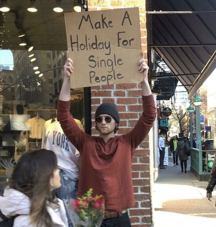 Person holding sign saying "Make a holiday for single people" in a city street, highlighting the single life experience.