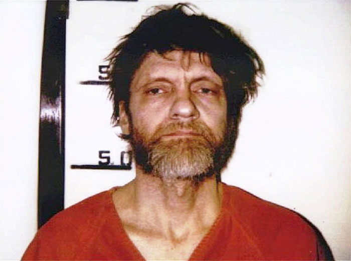 Mugshot of a man with unkempt hair and beard wearing a prison uniform related to conspiracy theories people believe in.
