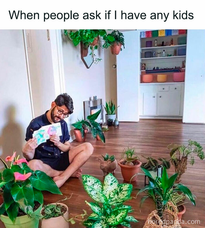Single person joyfully surrounded by houseplants, sitting on the floor and holding a plant care book.