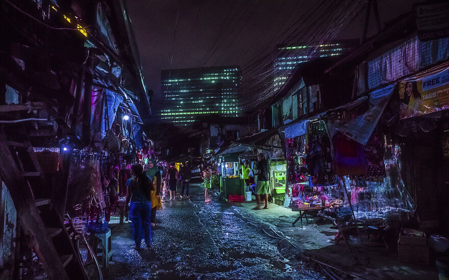 A Street Scene From The Same Slum, With Megacorp-Owned Buildings Towering Over It