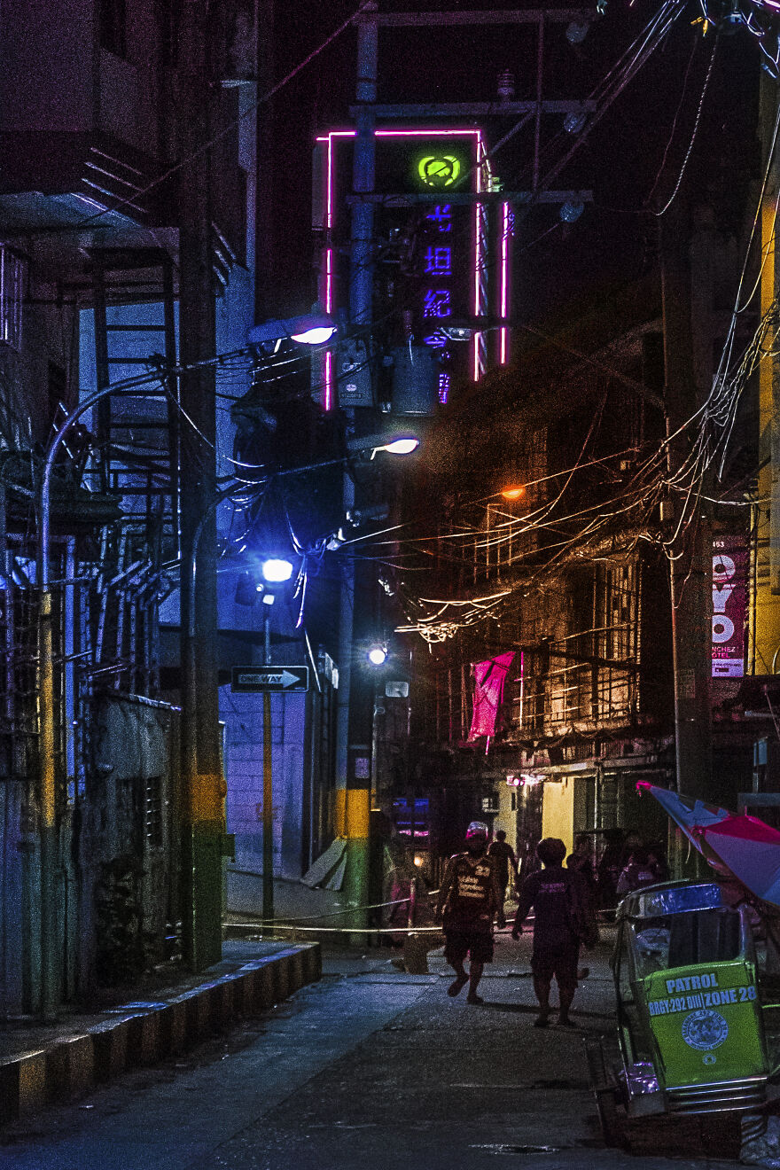 A Grimy Street In Binondo With A Neon Skyscraper Looming In The Distance