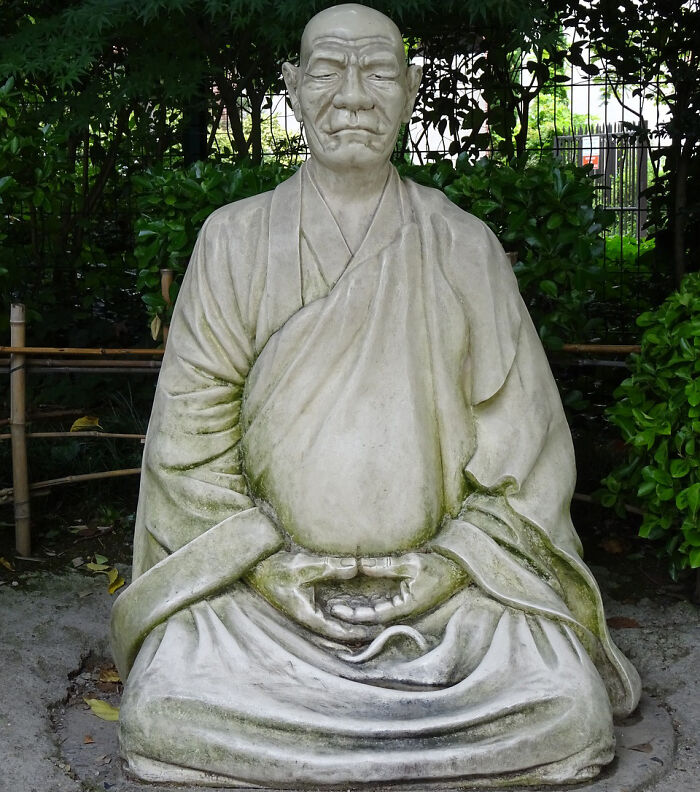 Stone statue of a meditating figure in a garden setting illustrating weird laws from around the world concept.