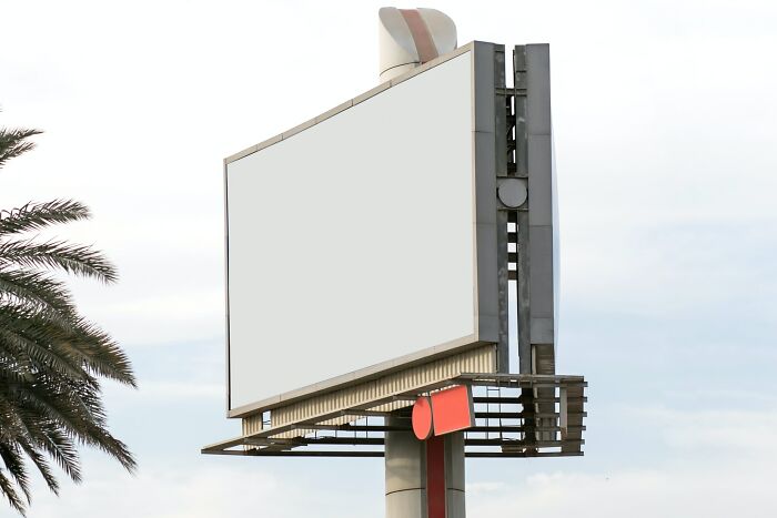 Large blank billboard on a tall pole near palm trees, illustrating weird laws from around the world concept.