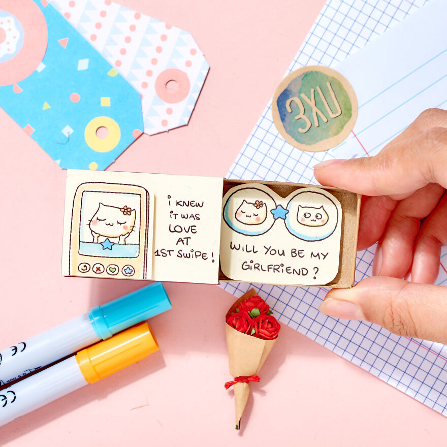 Hand holding a cute handmade card asking a girl to be your girlfriend, surrounded by colorful stationery and a small flower bouquet.