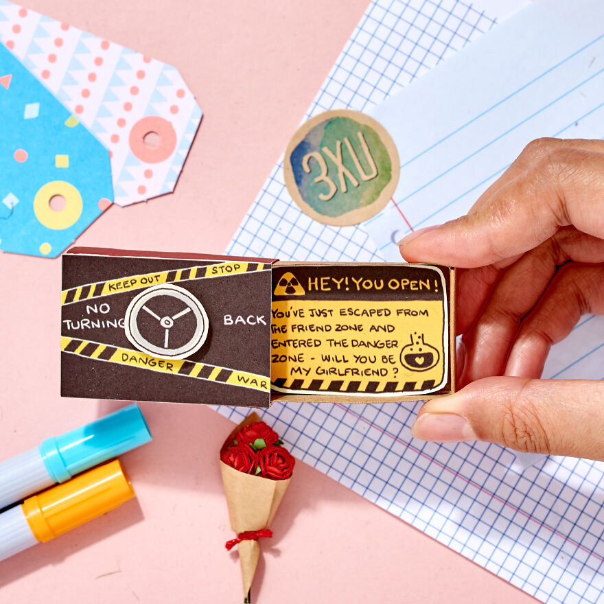 Hand holding a creative cute way to ask a girl to be your girlfriend with colorful markers and paper accessories nearby.