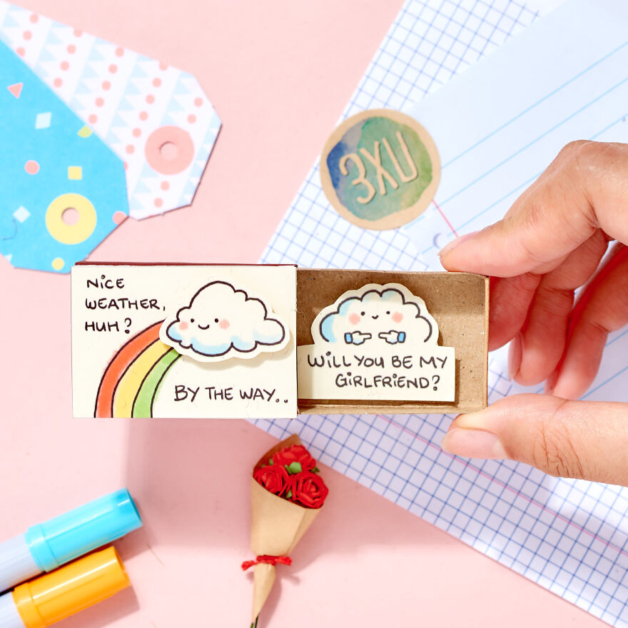 Hand holding a cute matchbox card with cloud illustrations and a question asking to be girlfriend in creative cute ways.