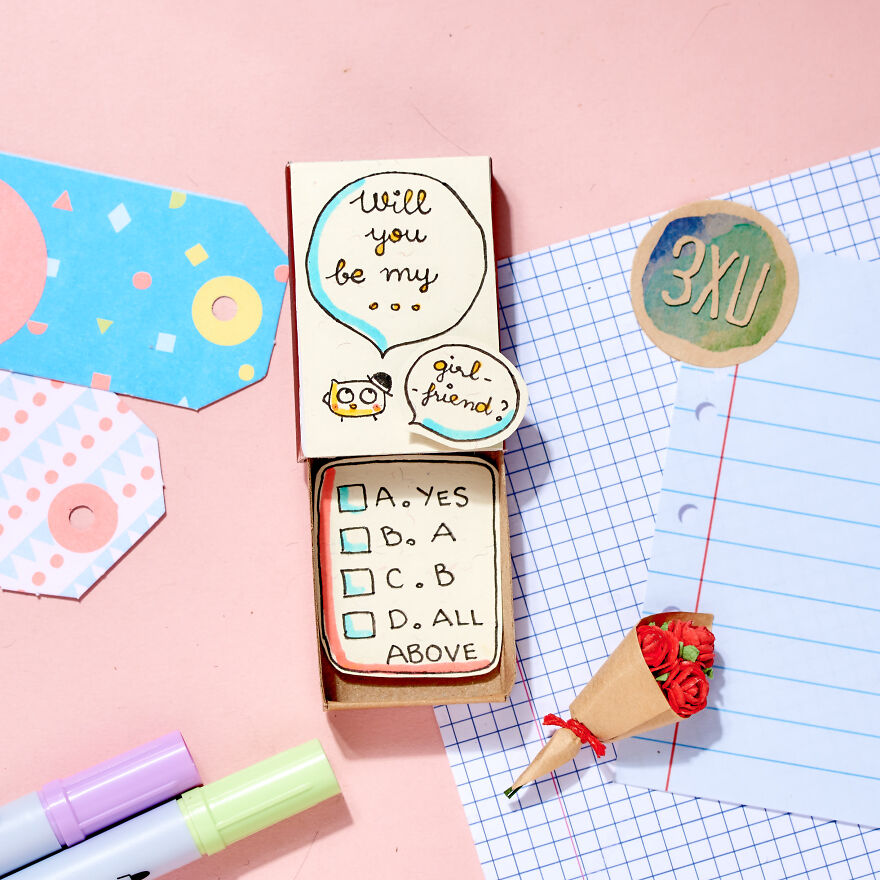 Cute handmade card asking to be girlfriend, displayed with colorful tags, tiny bouquet, and markers on pink background.