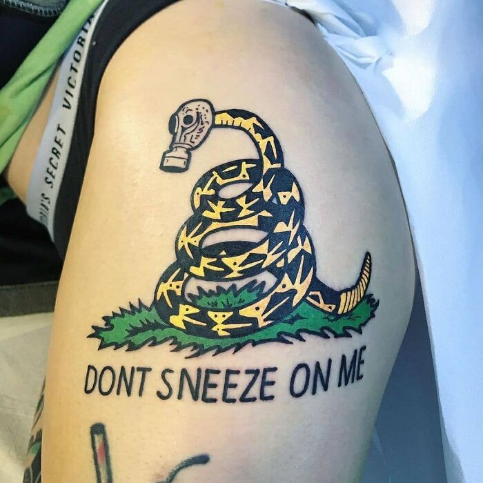 Outdated tattoo with snake and gas mask, reading "Don't Sneeze On Me," symbolizes irrelevant and uncool ink choices.