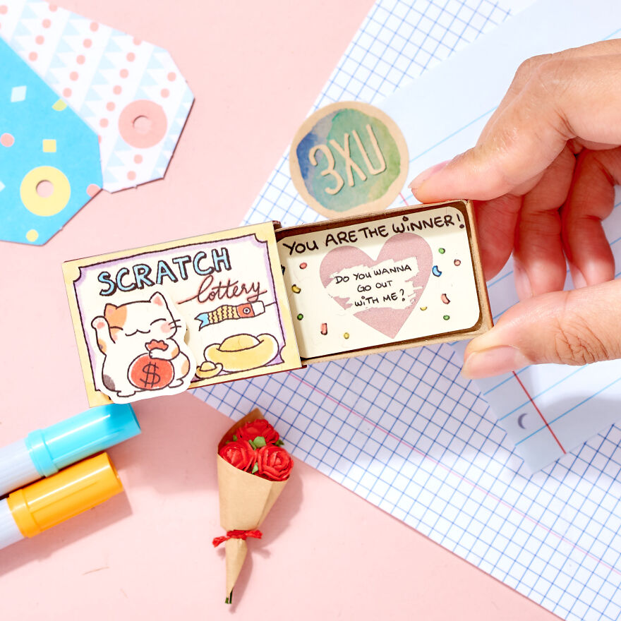 Hand holding a cute scratch lottery card asking a girl to be your girlfriend with small decorative items on a pink background.