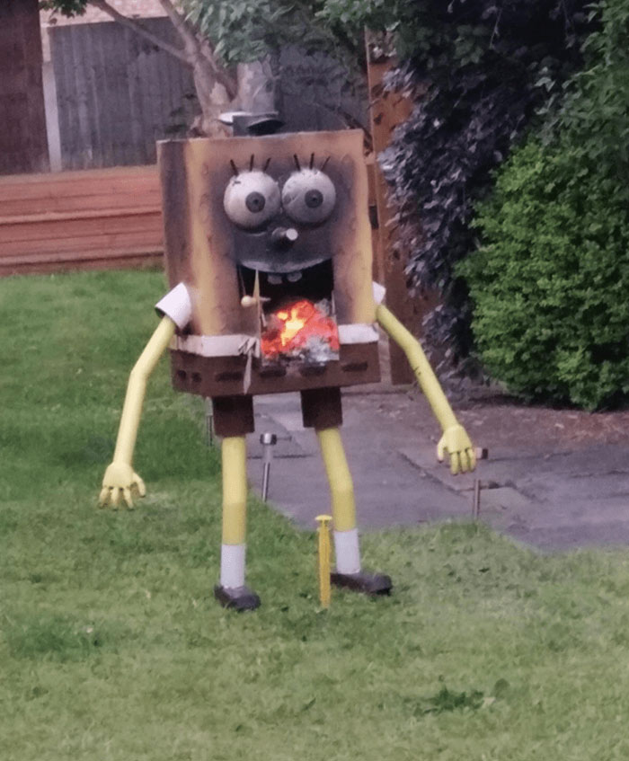 Knockoff brand sculpture resembling a cartoon character with square pants and a grill for a mouth, in a garden setting.
