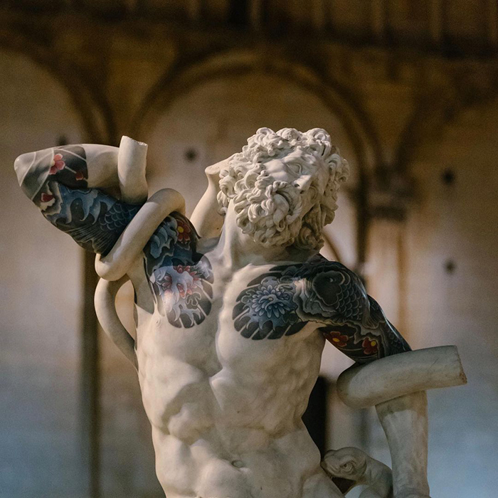 Sculpture with colorful tattoos highlighted by an Italian artist in a classic art setting.