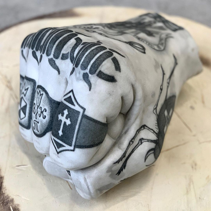 Tattooed sculpture by Italian artist, featuring intricate designs on a marble fist.