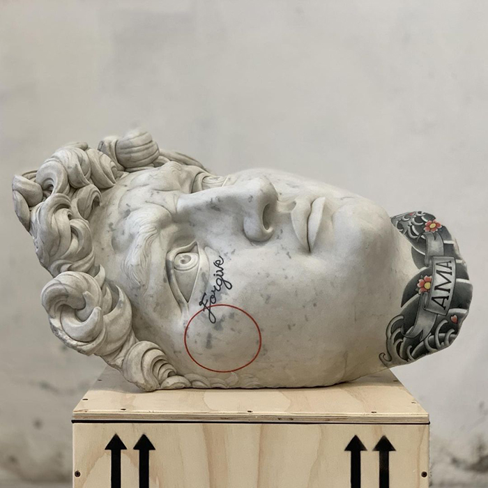 Sculpture head with tattoos by Italian artist, showcasing designs on stone instead of skin.