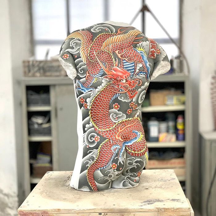 Italian sculpture with vibrant dragon tattoo design in a workshop setting.
