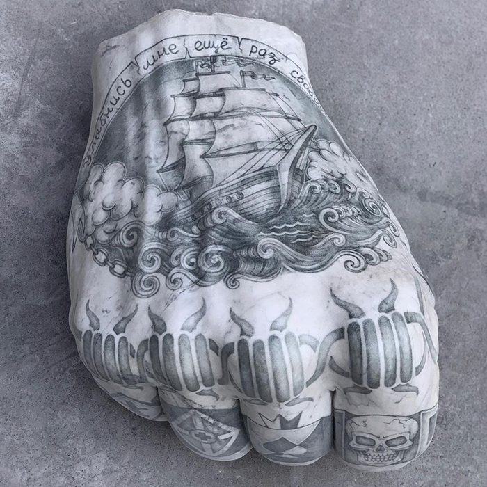 Tattooed sculpture of a ship on marble hand by Italian artist, showcasing art beyond skin.