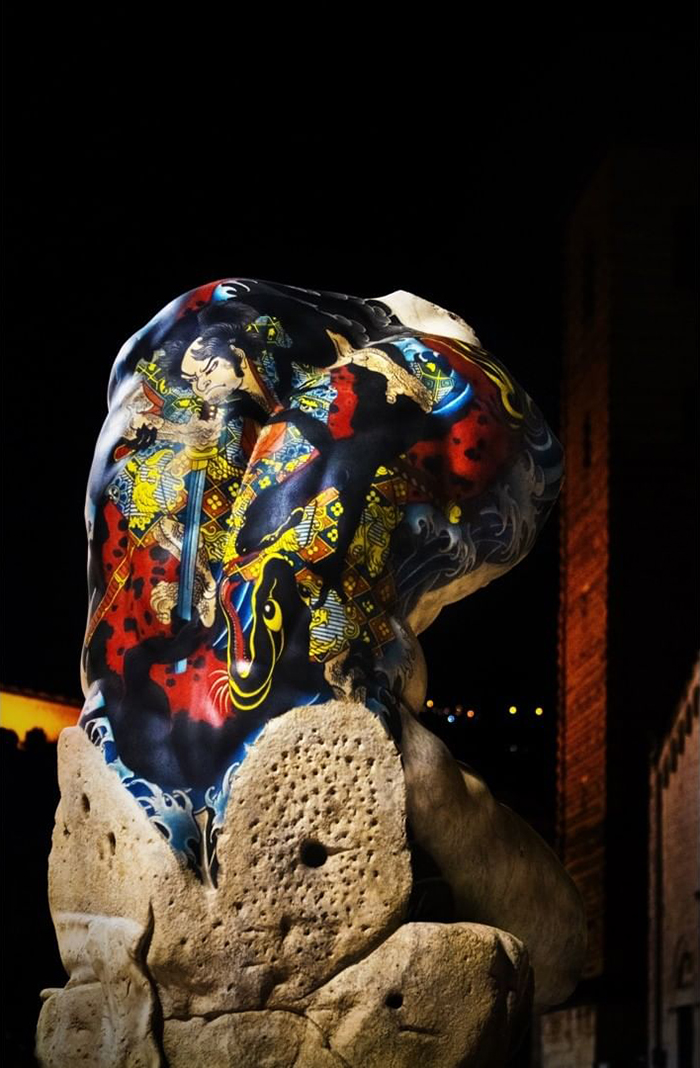 Italian artist's colorful tattoo on a sculpture enhances abstract form and vivid details against a dark background.