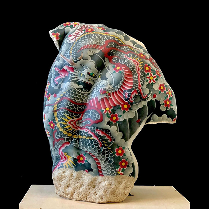 Tattooed sculpture by Italian artist featuring vibrant dragon and floral designs on a stone bust.